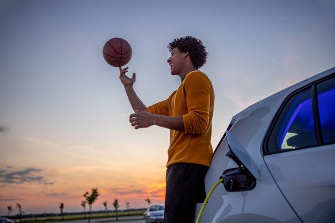 © Getty Images/SimonSkafar Mann dreht Basketball auf Fingerspitze und steht vor einem Sonnenuntergang angelehnt am ladenden Auto