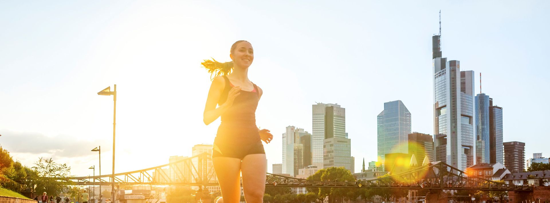 © Westend61 via Getty Images Frau joggt lächelnd am Main vor der Frankfurter Skyline