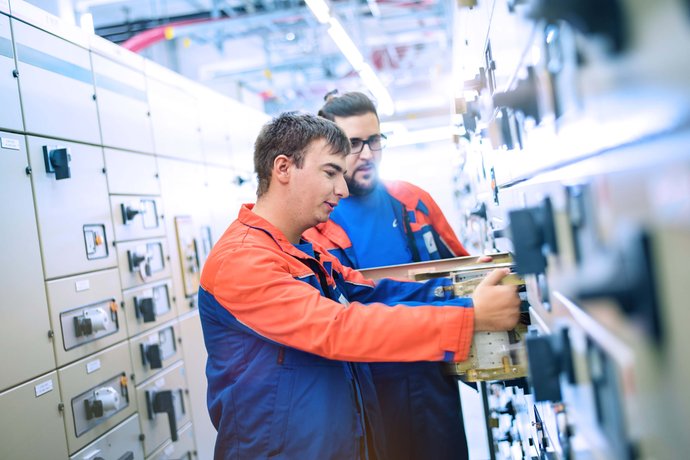 Zwei Techniker vor einer Schaltanlage und tauschen ein Modul aus