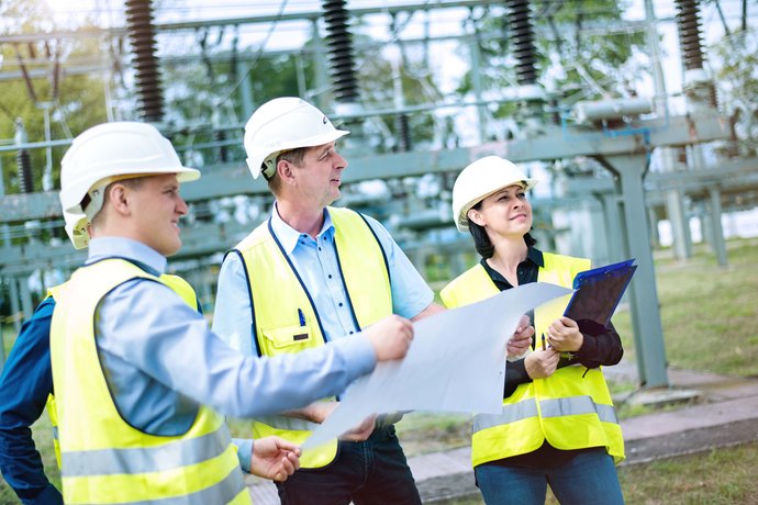 Zwei Männer und eine Frau mit Architektenplan in der Hand bei einen Umspannwerk