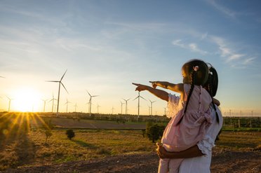 Mutter mit Tochter auf dem Arm schauen zu einem Windpark bei Sonnenaufgang