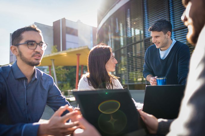 Gruppe mit Studierenden sitzt draußen in der Sonne und redet miteinander