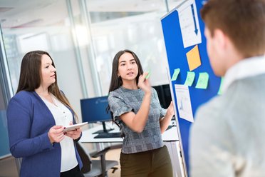 Zwei Frauen und ein Mann diskutieren miteinander vor einer Pinwand.