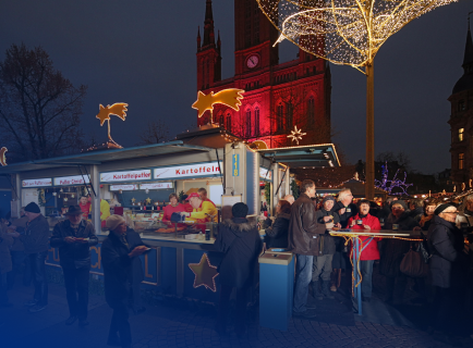 Menschen an einem Stand für Kartoffelpuffer auf dem Weihnachtsmarkt