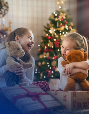 Zwei kleine Mädchen spielen und kuscheln mit ihren Teddybären vor einem Weihnachtsbaum