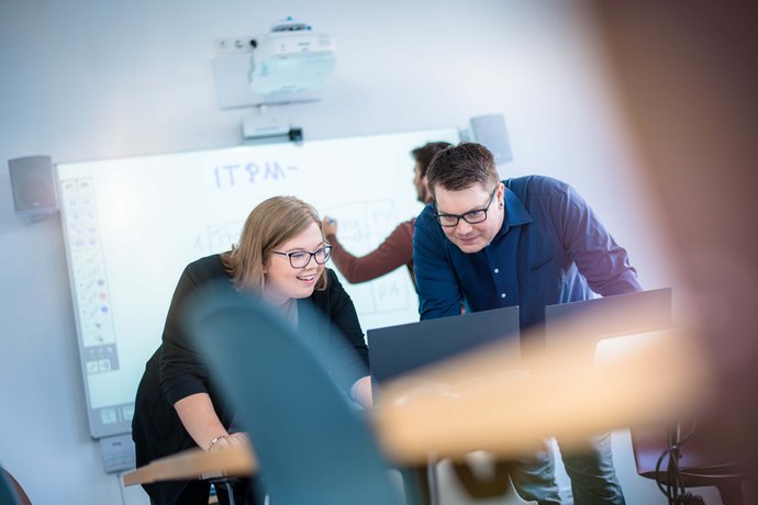 Zwei Auszubildende lehnen sich am Tisch über ein Notebook und betrachten den Monitor