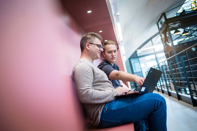 Ausbilder sitzt mit Notebook und bekommt vom Auszubildenden etwas am Monitor gezeigt