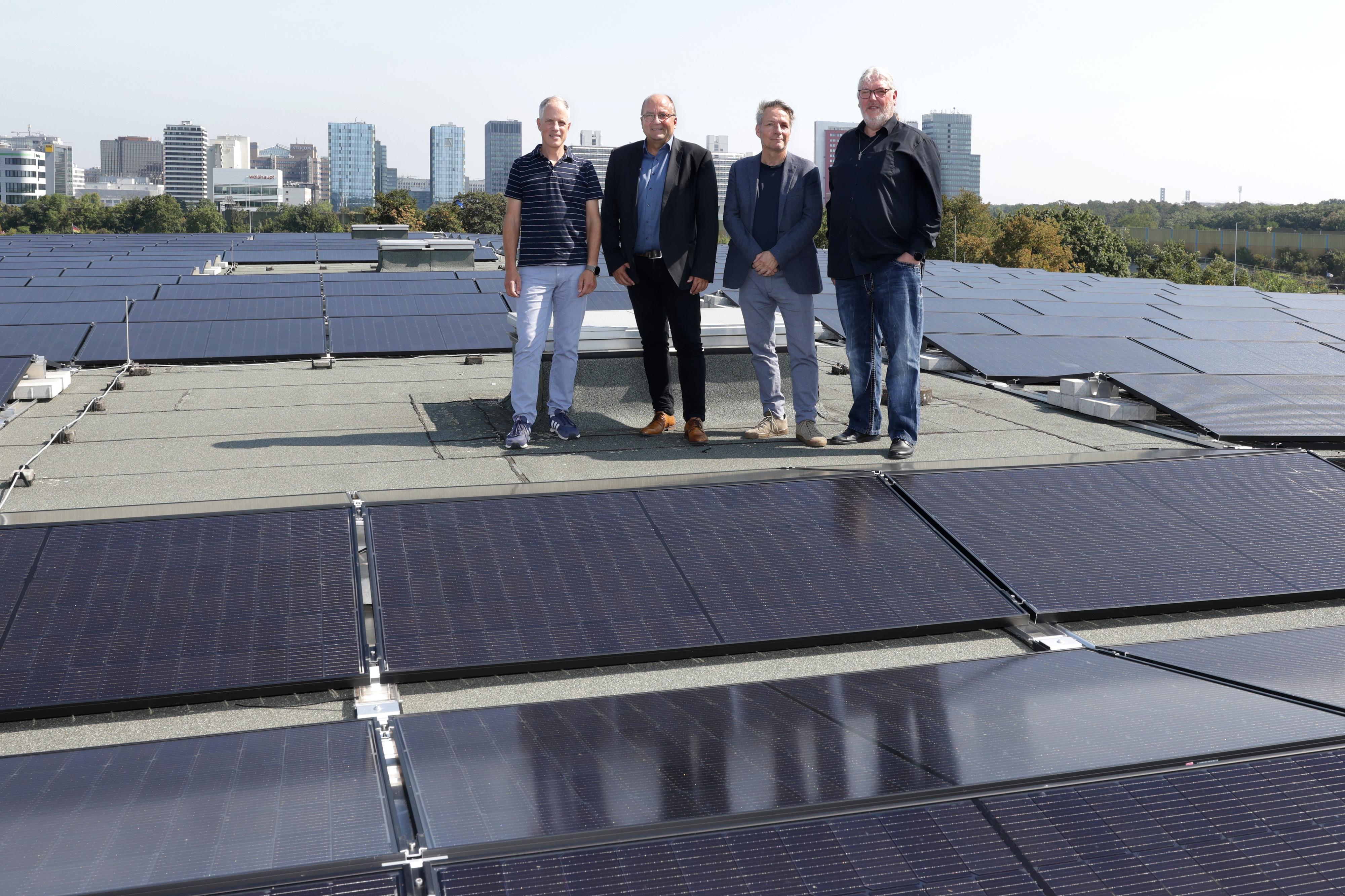 Vier Männer stehen auf einem Dach umgeben von Solarmodulen