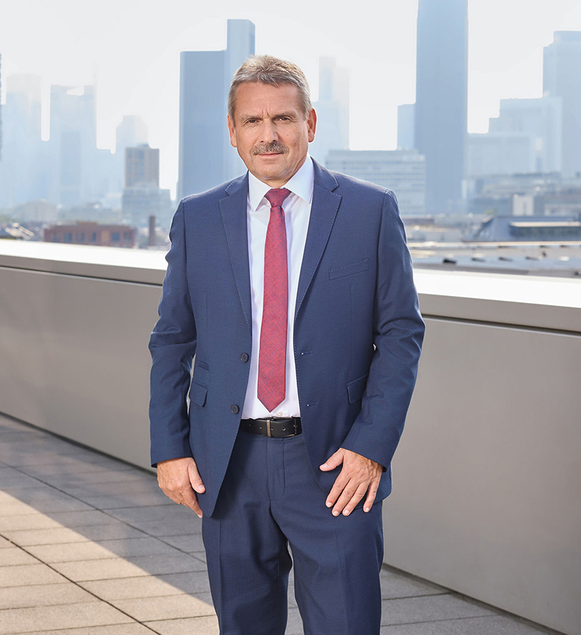 Mann im blauen Anzug mit roter Krawatte steht auf einer Terrasse vor einer Skyline. Professioneller, formeller Ausdruck.