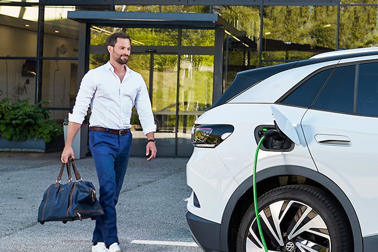 Junger Mann geht auf sein E-Auto zu, das gerade an einer Ladesäule aufgeladen wird.