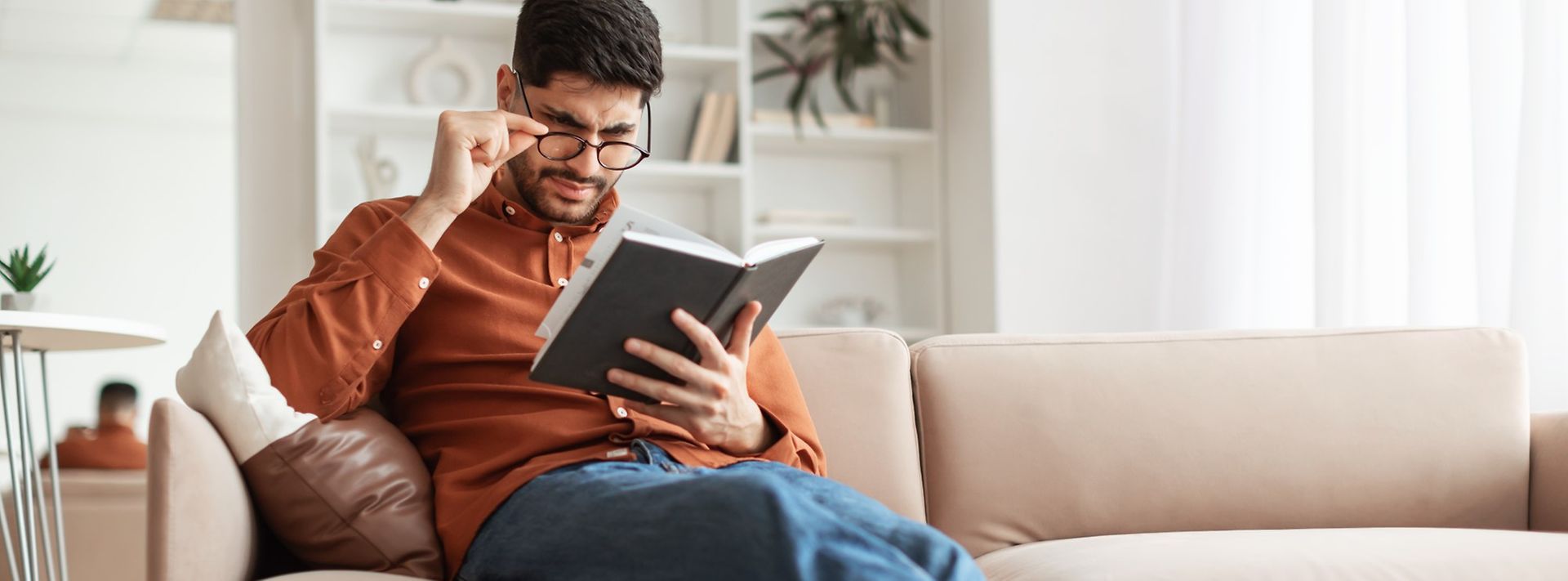 Junger Mann sitzt auf dem Sofa und liest ein Buch.