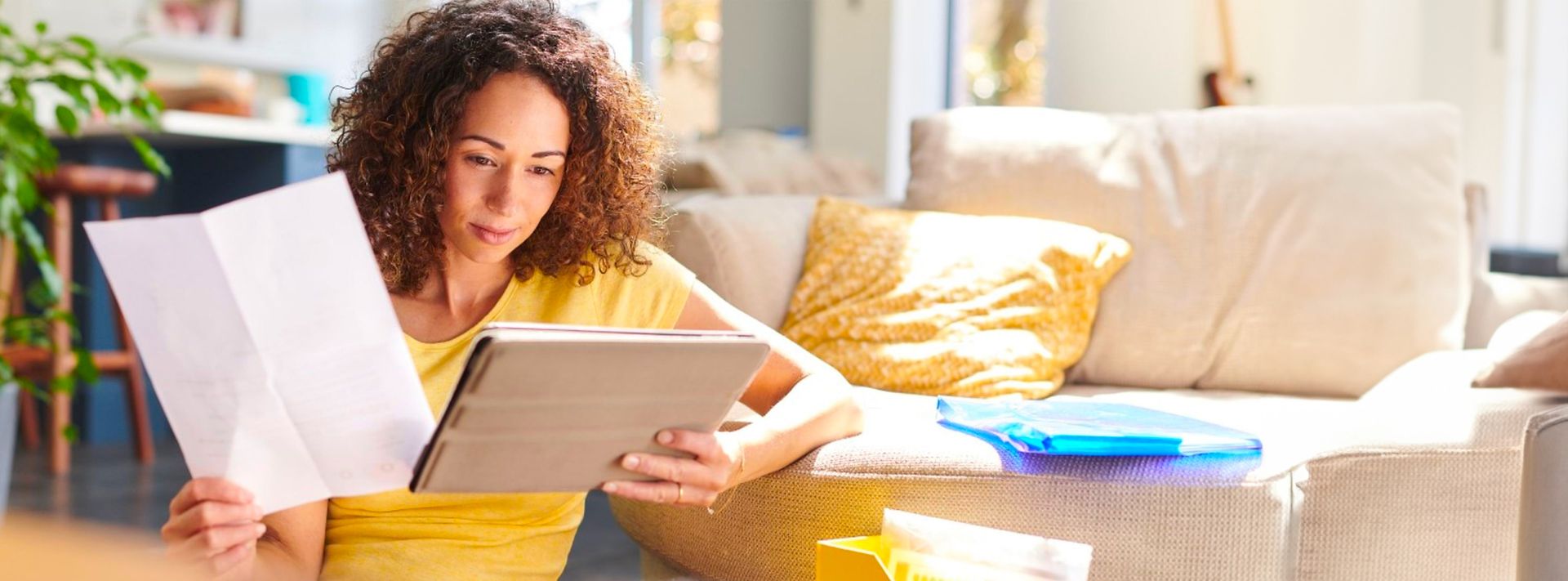 Frau sitzt vor Couch und schaut auf Tablet mit Dokument in der Hand