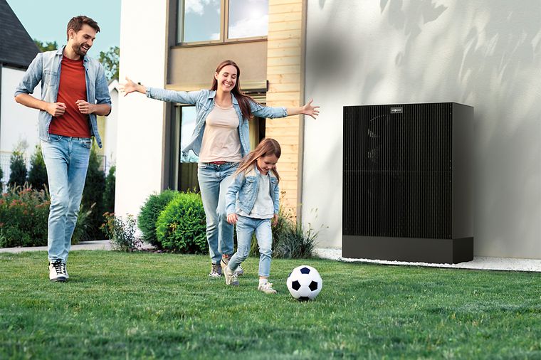 Eltern und Tochter spielen Fußball im Garten, das Mädchen rennt mit Ball vorneweg