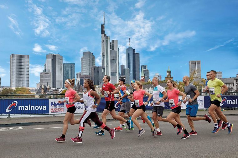 Läufergruppe vor der Frankfurter Skyline und vor Zaun mit Mainova Banner