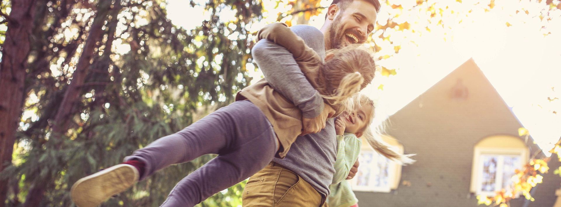 Vater hebt Kinder hoch lachend im Garten