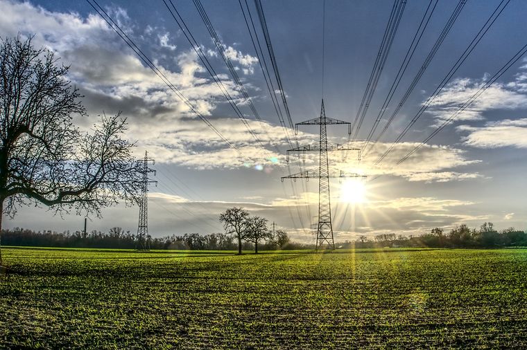 Freileitungsmasten auf einem Feld, Sonne strahlt am Himmel