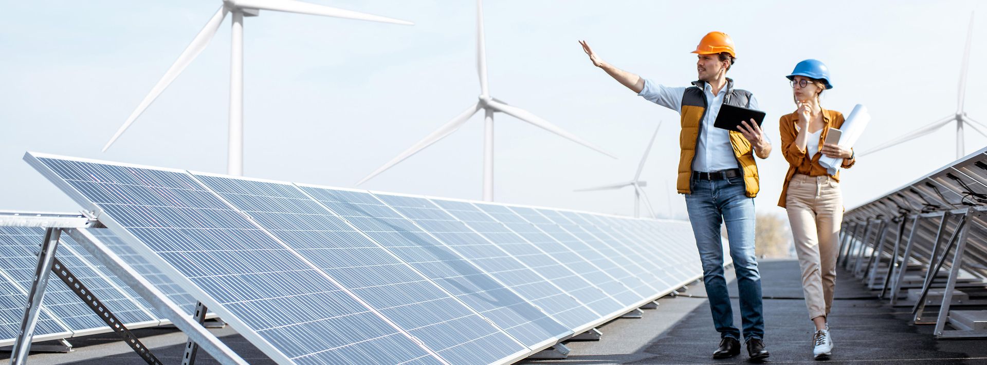 Geschäftsleute begutachten Photovoltaikanlage auf dem Dach eines Gebäudes mit Windrädern im Hintergrund