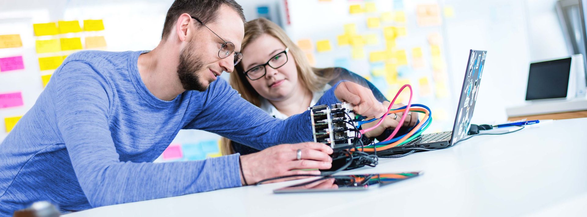 Ausbilder erklärt Auszubildende ein elektronisches Gerät was auf dem Tisch liegt